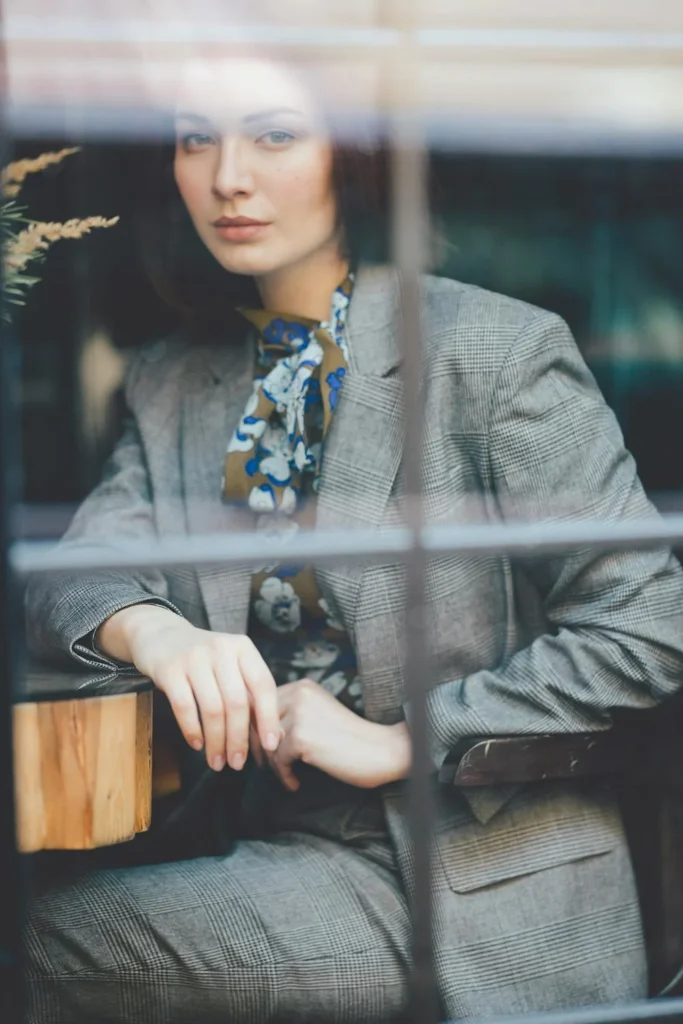 Elegant woman in a tailored navy blue pantsuit, accessorized with a pearl necklace and matching earrings, standing confidently in a modern office setting