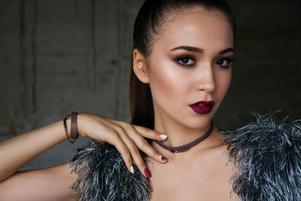 Close-up of a woman with an elegant updo hairstyle, featuring soft curls and subtle highlights, complemented by flawless makeup with smoky eyes, defined brows, and a nude lipstick